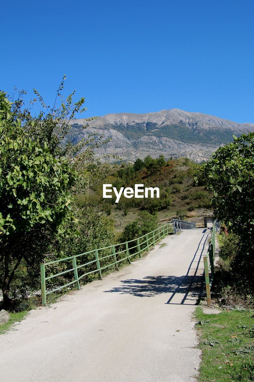 plant, tree, nature, mountain, sky, scenics - nature, clear sky, no people, beauty in nature, landscape, environment, blue, day, road, rural area, the way forward, outdoors, land, sunny, mountain range, footpath, tranquility, tranquil scene, transportation, non-urban scene, sunlight, travel, travel destinations, architecture
