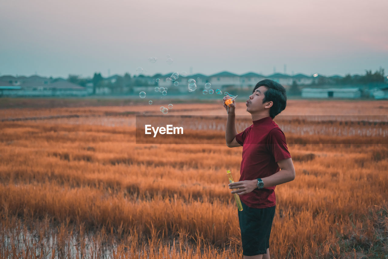 Side view of man blowing bubbles while standing rice farm