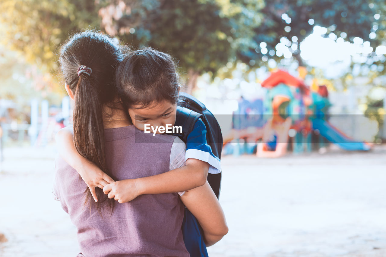 Rear view of mother carrying daughter while standing in playground