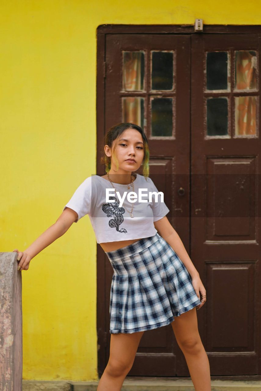 Portrait of beautiful young woman standing against yellow wall