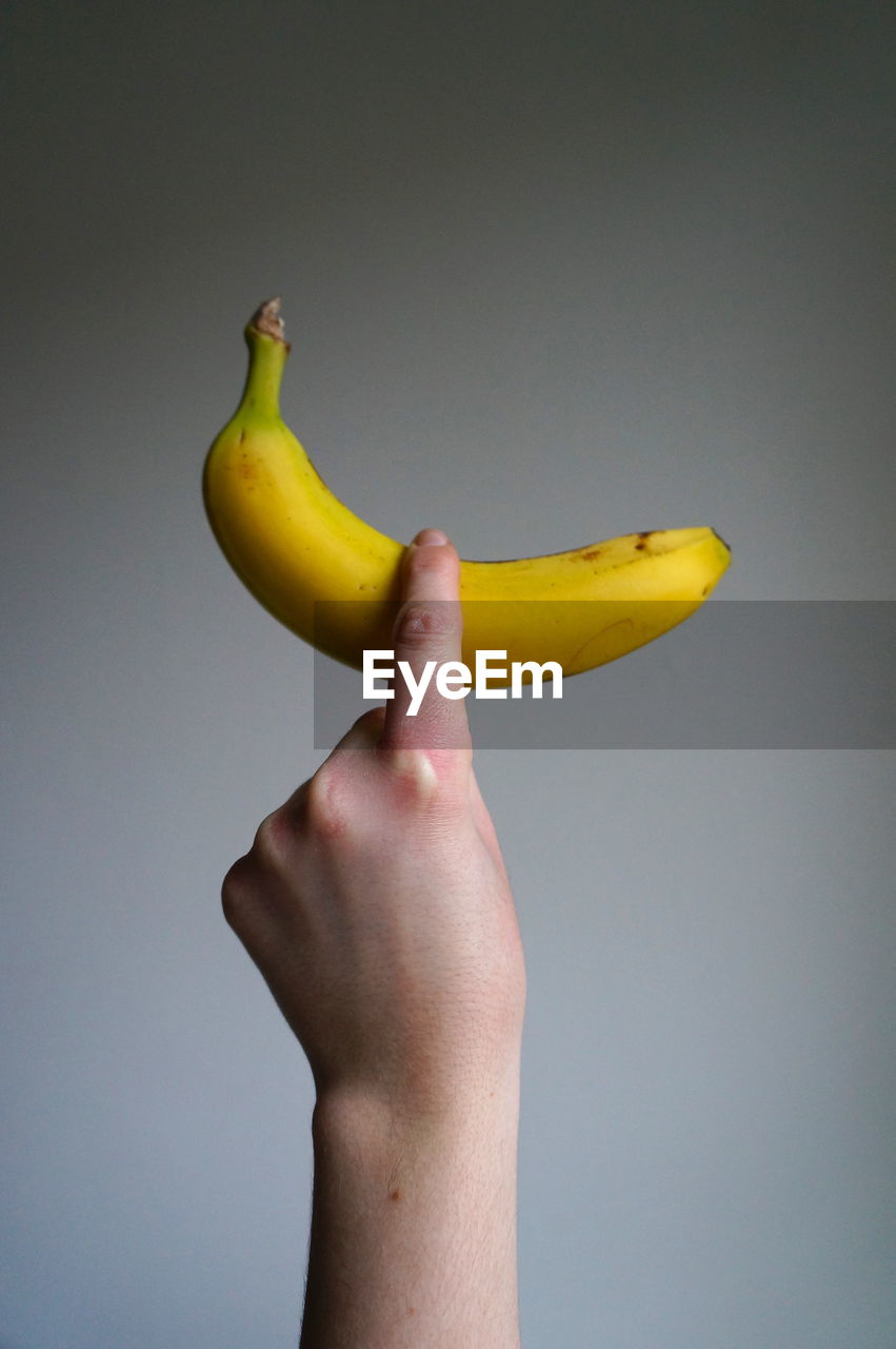 Cropped image of hand holding banana against gray background