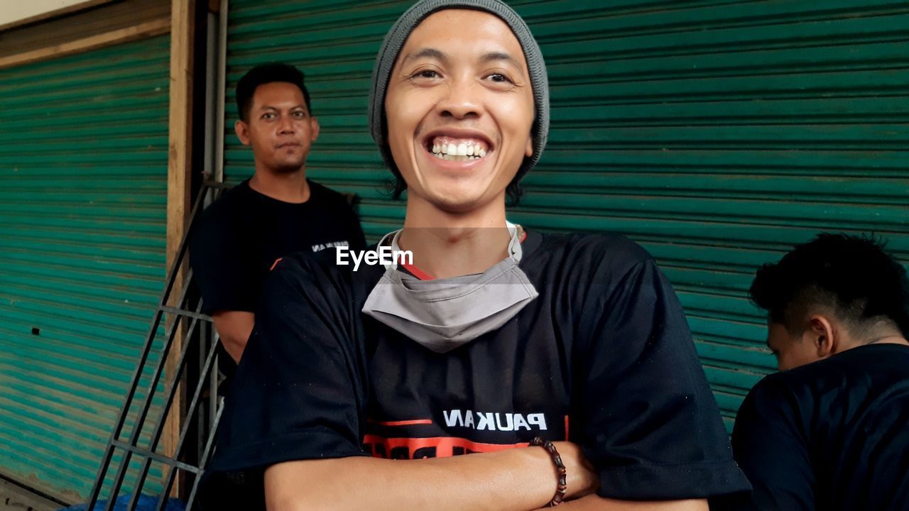 PORTRAIT OF A SMILING YOUNG MAN STANDING AGAINST BLUE WALL