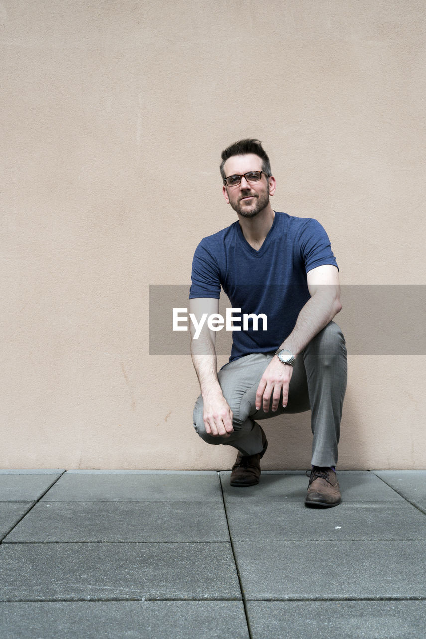 Young man crouching against wall