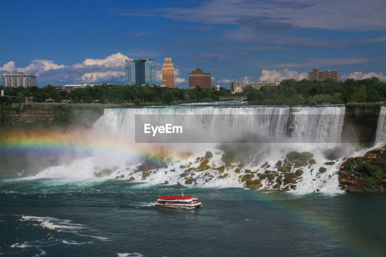 View  of american falls with a rainbow and a cruise boat moving in the water of niagara falls.