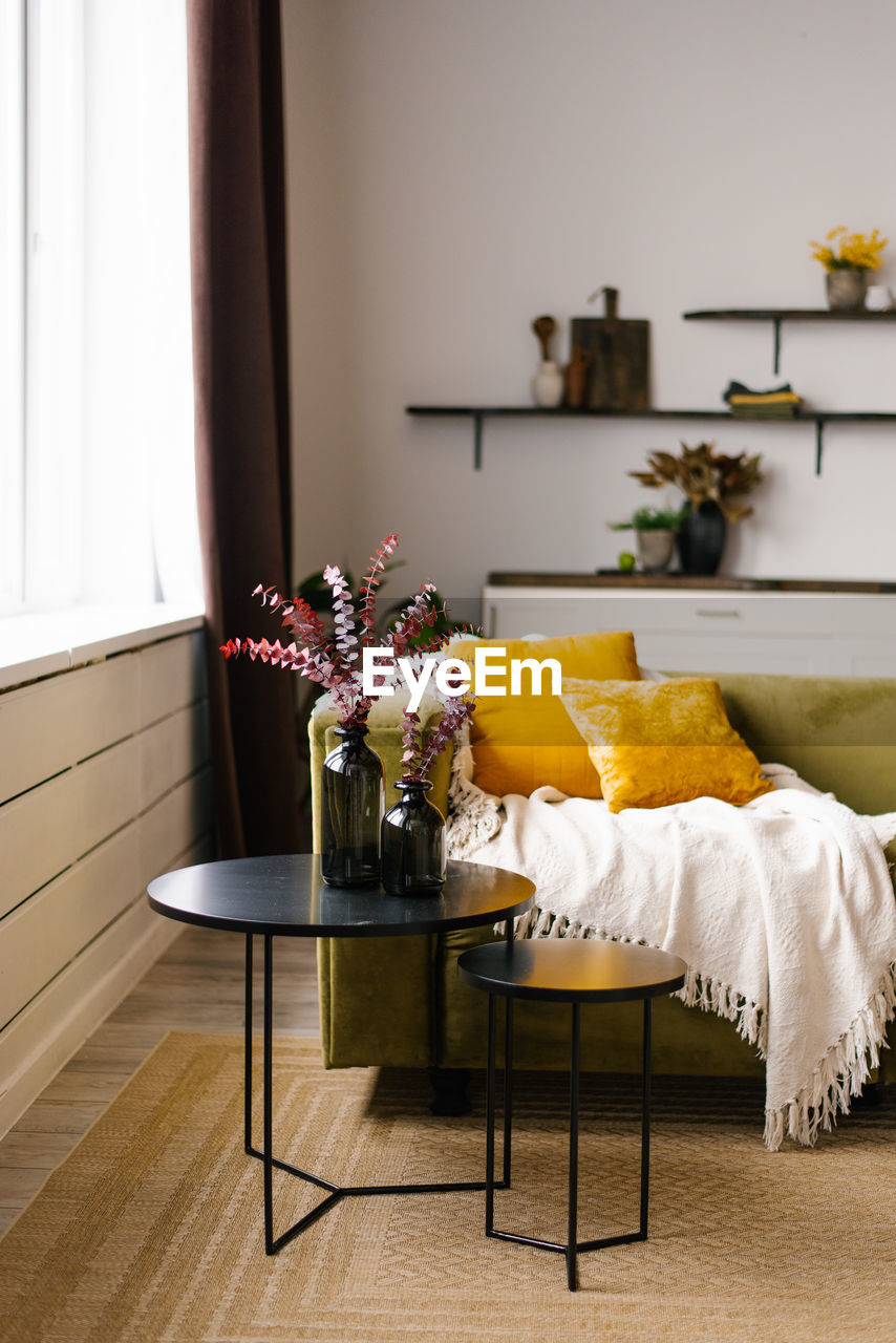 A green sofa with yellow pillows and a double black coffee table and a blanket in a living room