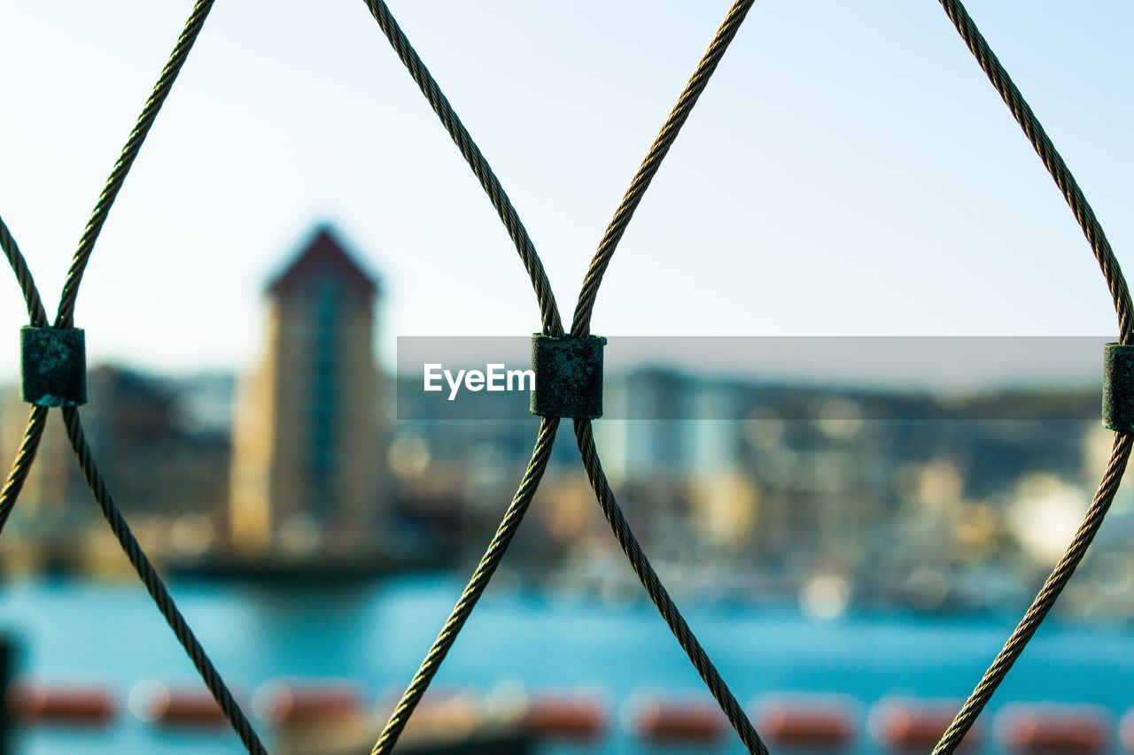 Close-up of fence by city against sky