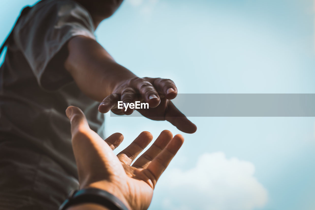 Cropped image of man reaching towards girlfriend hand against sky