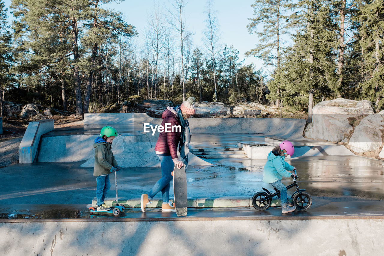 Mom and her kids walking across a skatepark with bikes and scooters