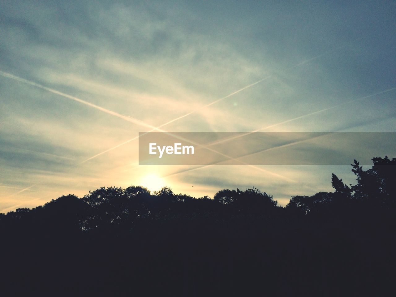 Low angle view of vapor trails in cloudy sky during sunset