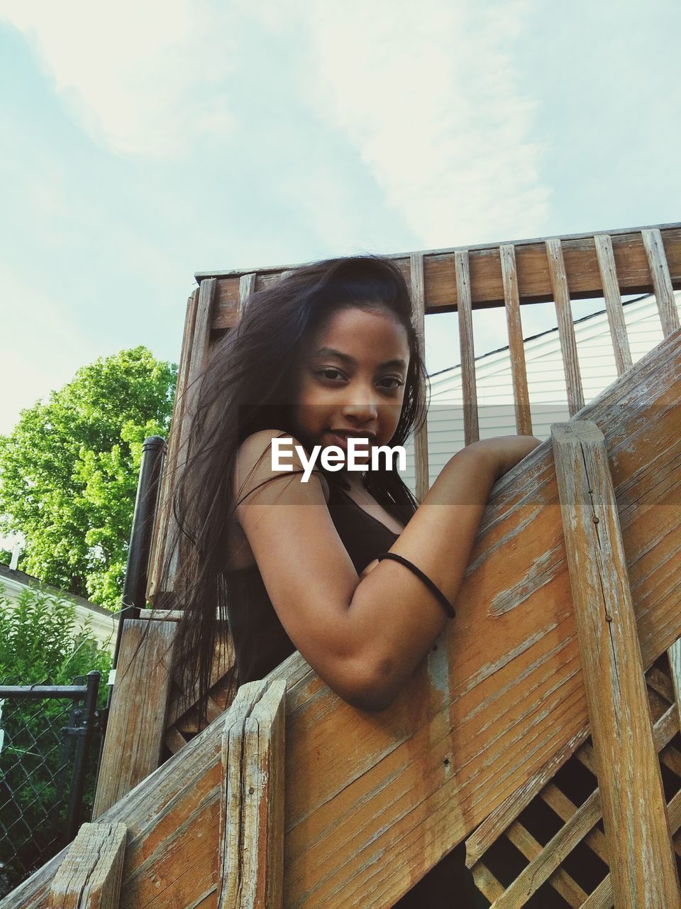 Portrait of smiling young woman sitting on railing against sky