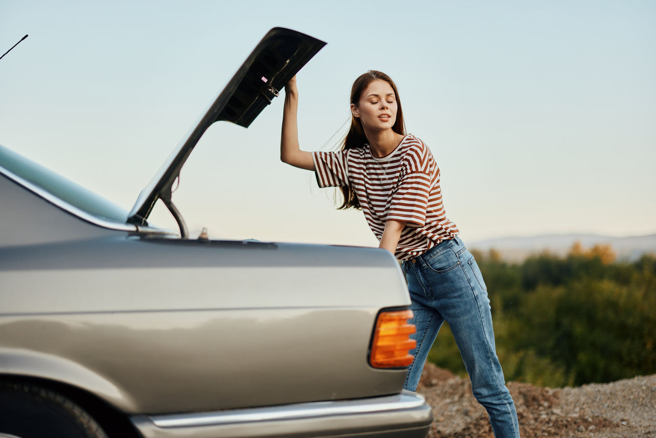 rear view of young woman standing against car