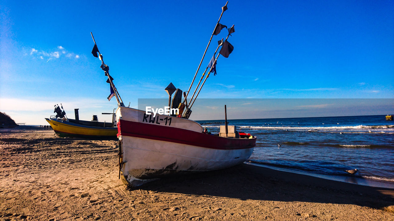 FISHING BOATS MOORED ON SHORE AGAINST SKY