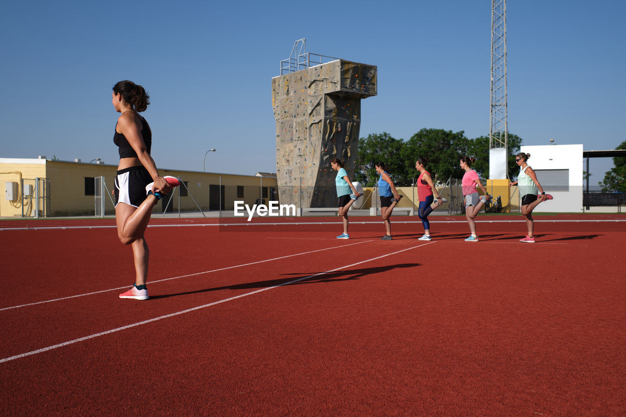 Group of women practice pre-workout stretching with their young traine