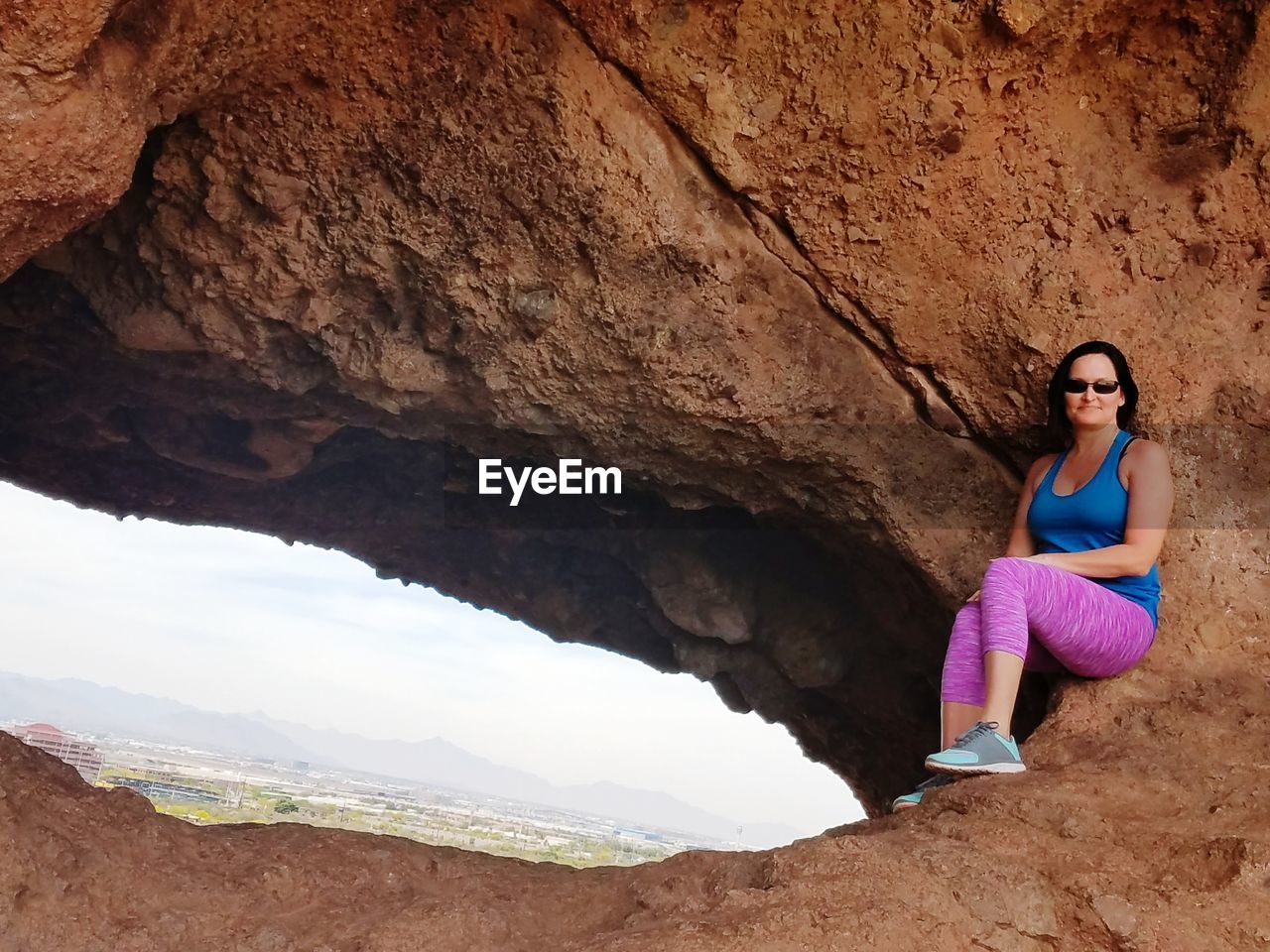 Smiling woman in sunglasses sitting on rock