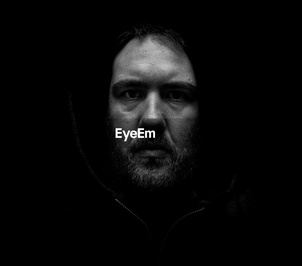 Close-up portrait of young man wearing hood against black background