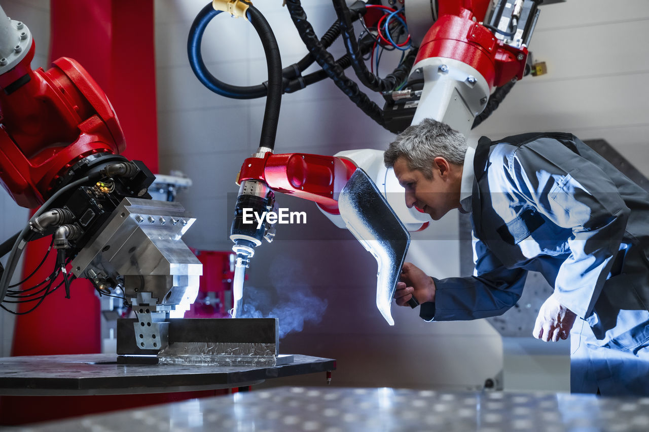 Mature worker with welding helmet working at robotics in factory