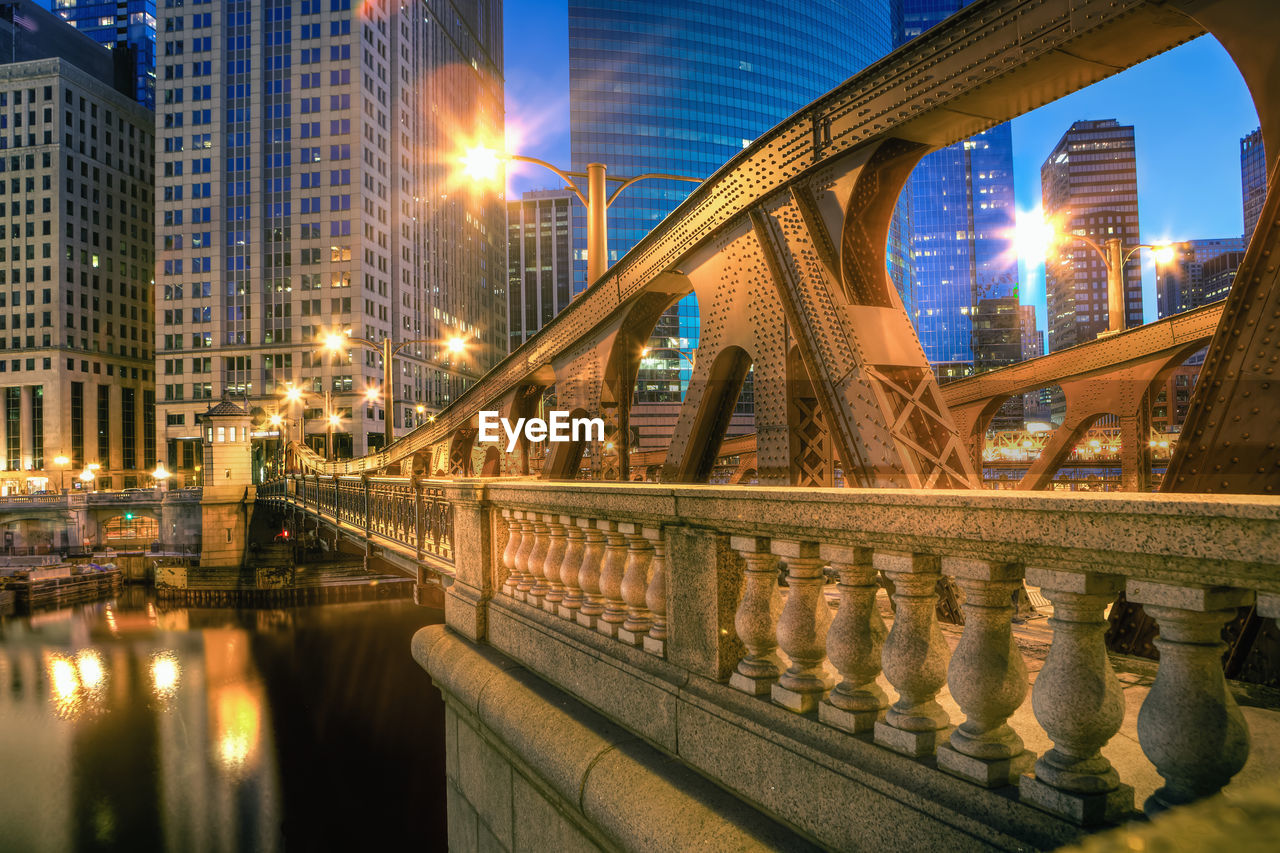 Illuminated bridge over river by buildings in city at night