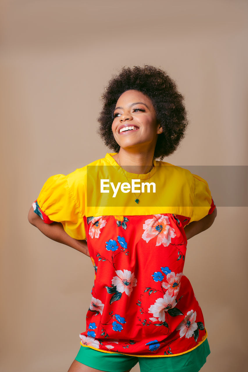 Portrait of young woman standing against yellow background