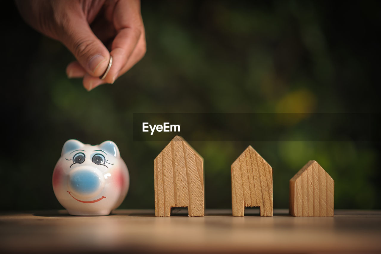 Cropped hand putting coins in piggy bank by model houses on table