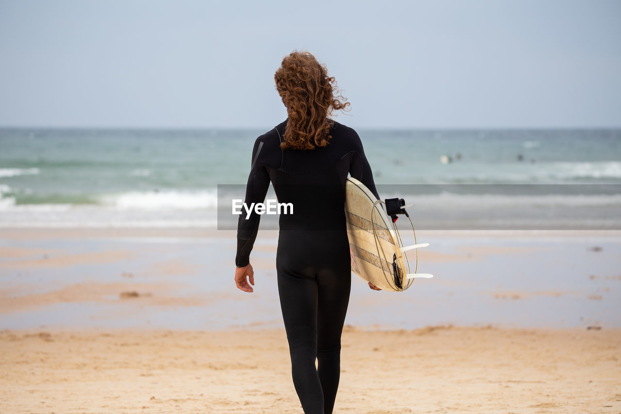 REAR VIEW OF A WOMAN WALKING ON BEACH