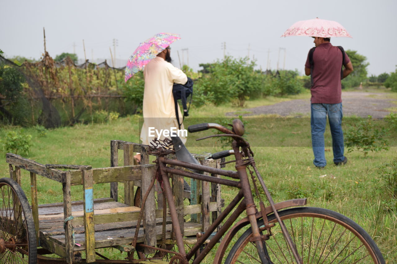 Rear view of men with umbrellas standing on grassy field