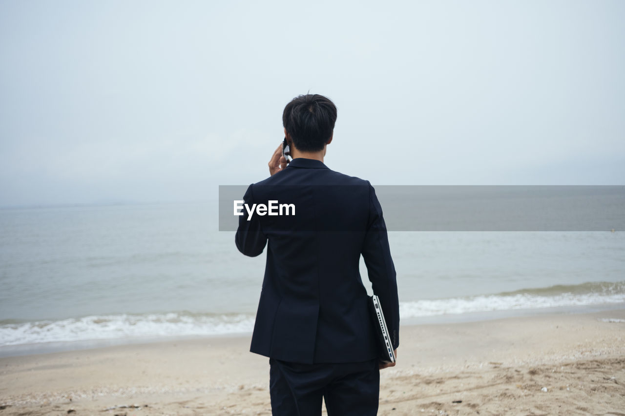 REAR VIEW OF MAN LOOKING AT BEACH