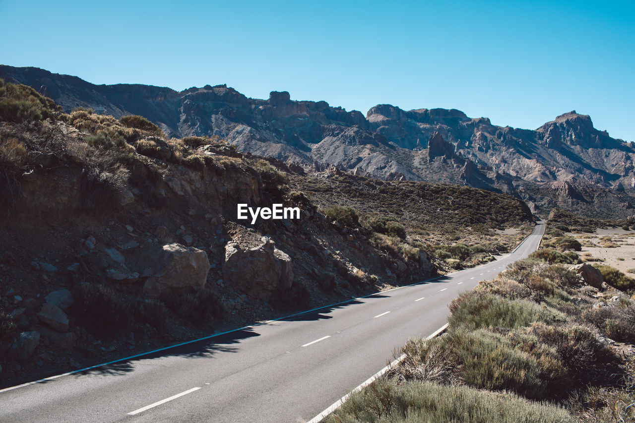 Road leading towards mountains against clear sky