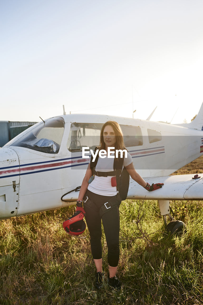 Young female skydiver in an airfield with a plane behind her