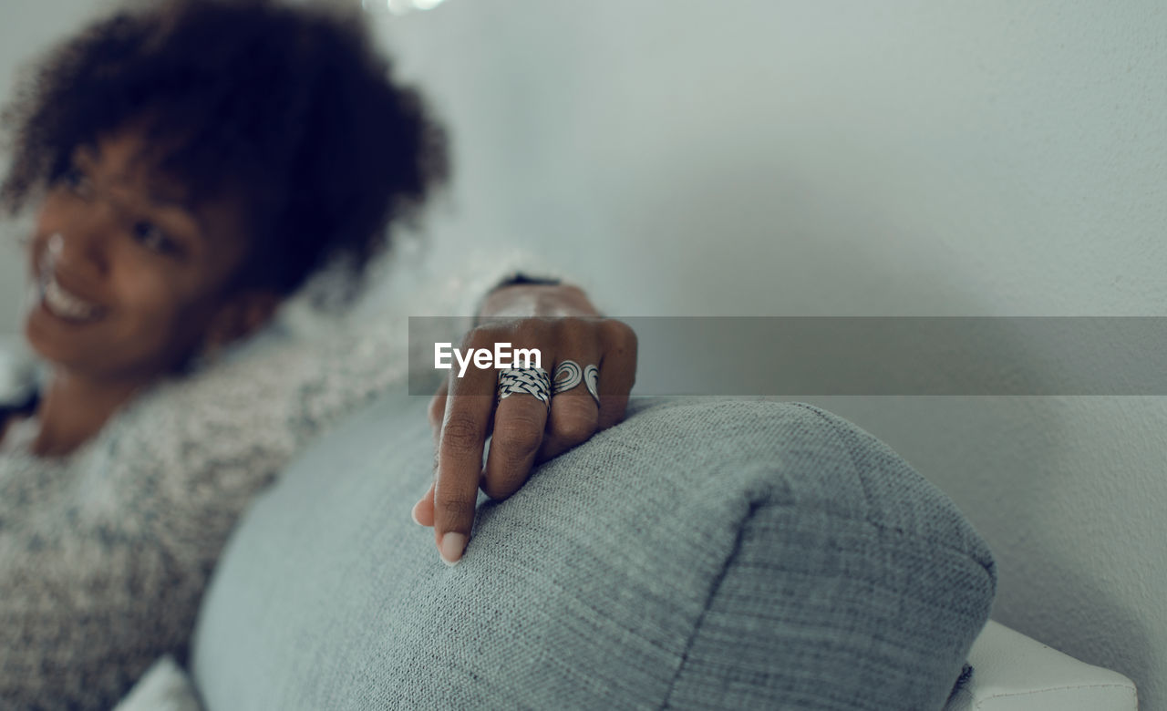 Selective focus on the hand with rings of a smiling black woman sitting on a couch