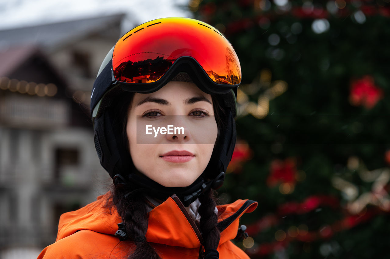Portrait of attractive caucasian young woman skier in helmet with ski mask against green christmas