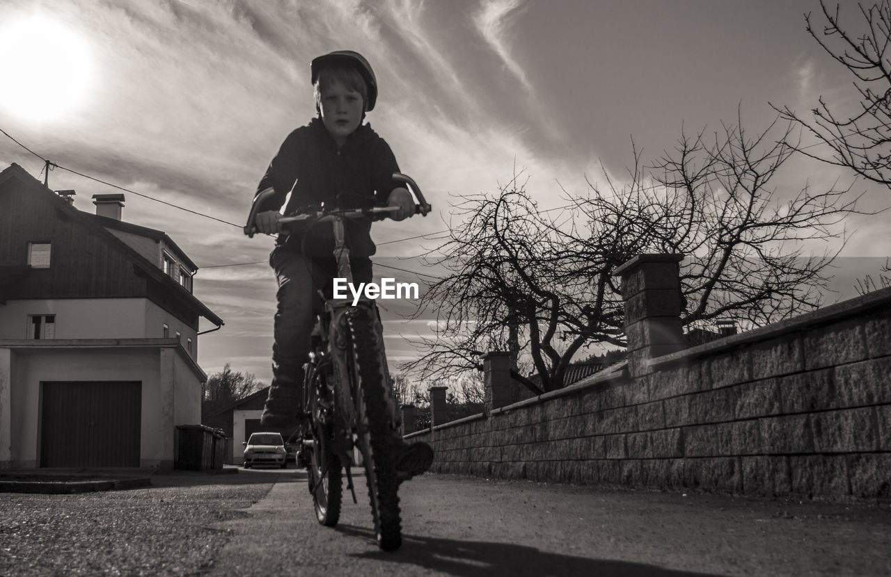 Low angle portrait of boy cycling on footpath against sky