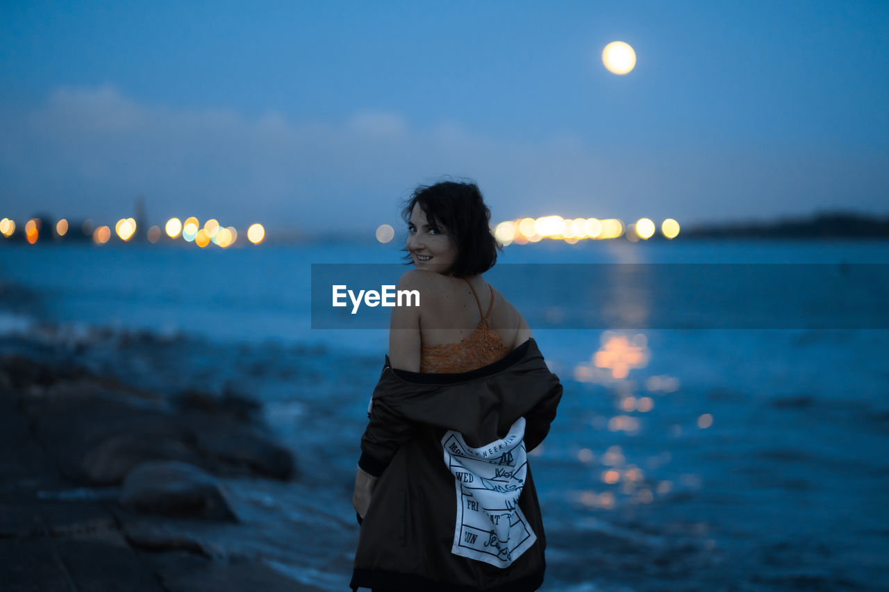 Portrait of smiling woman standing at beach against sky