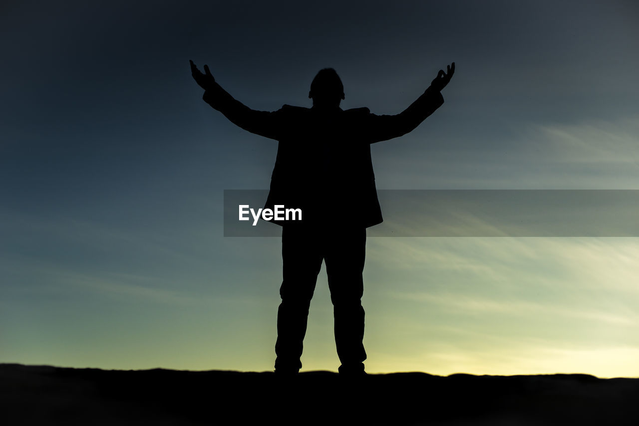 SILHOUETTE OF WOMAN WITH ARMS RAISED AGAINST SKY