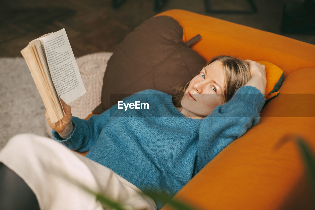 A beautiful girl is relaxing on the sofa in the living room, reading her favorite novel. 