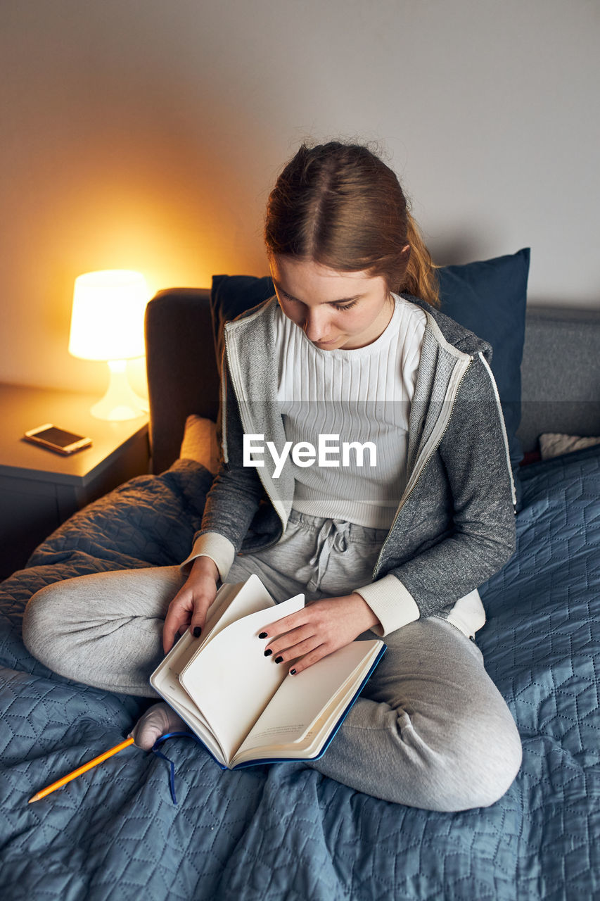 Student learning at home. young woman making notes, reading and learning from notepad sitting in bed