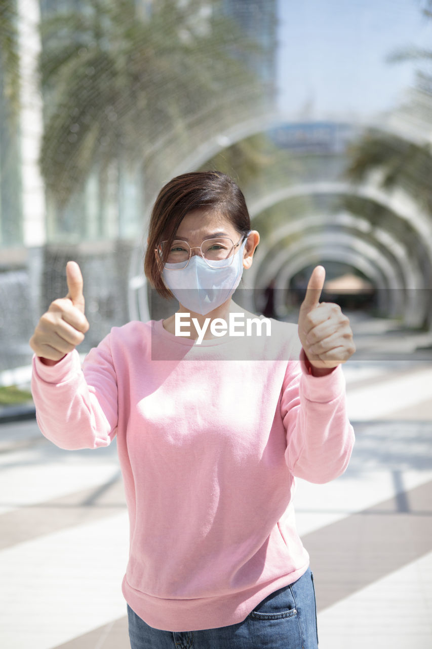 Woman wearing protection mask standing outdoor raising hand for good healthy