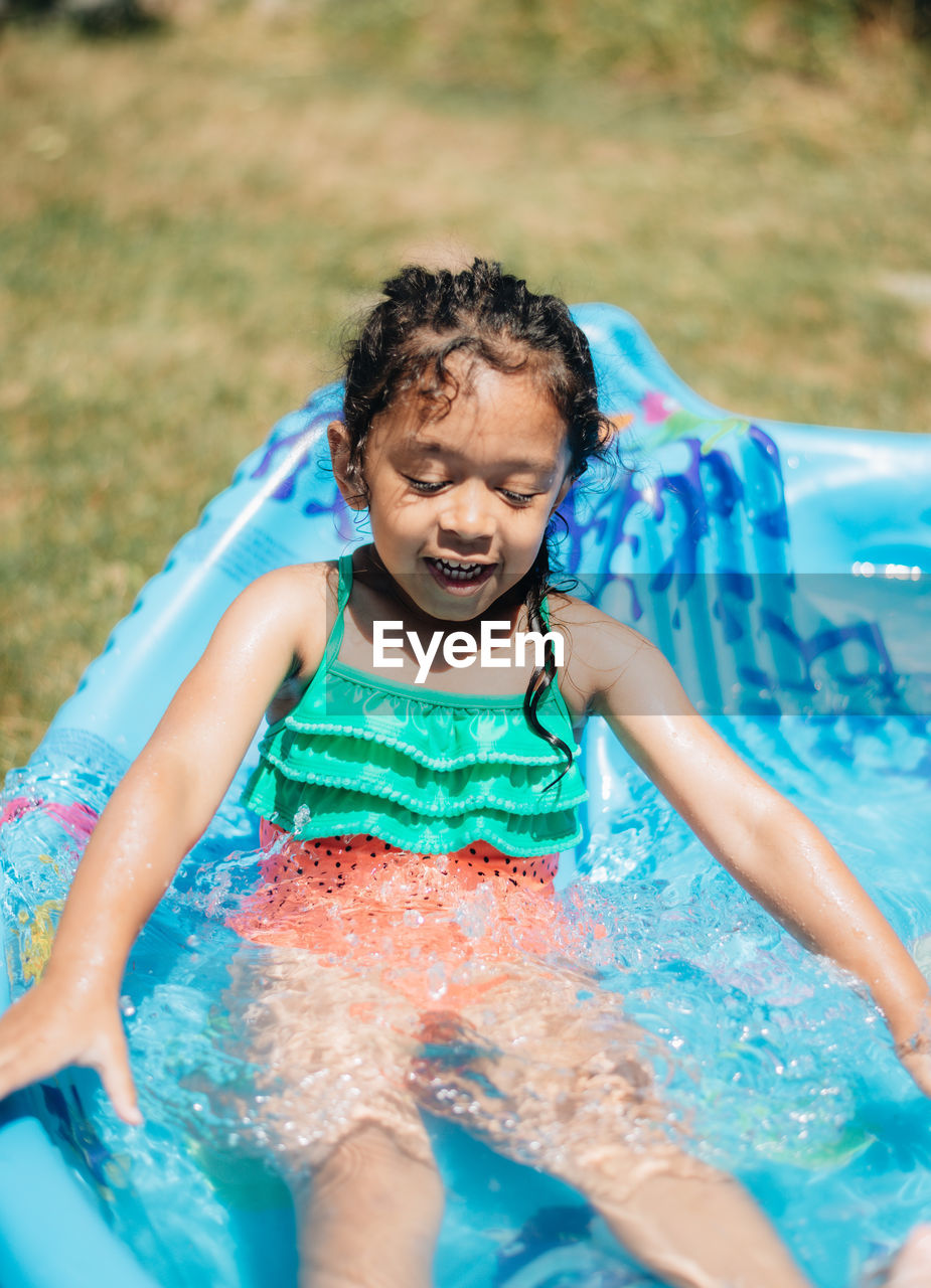 Mixed race young girl at home having fun on hot summer day in kiddie pool