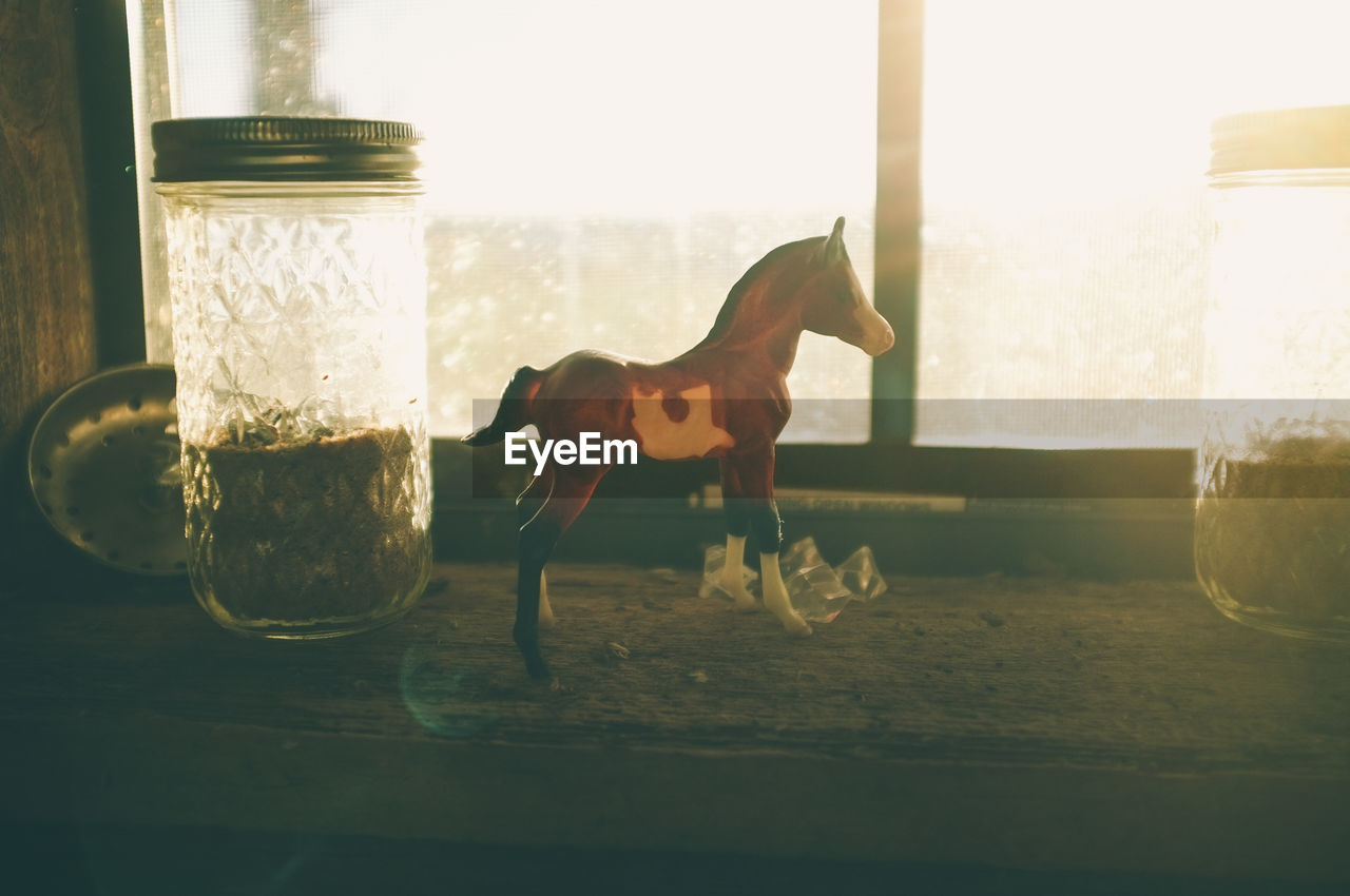 Close-up of horse toy on table against window at home