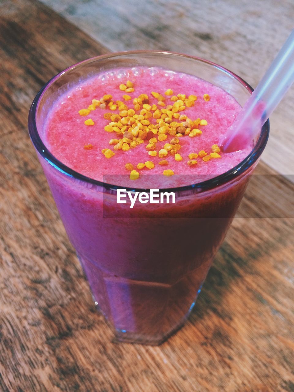 High angle view of bee pollen smoothie in drinking glass with straw on table