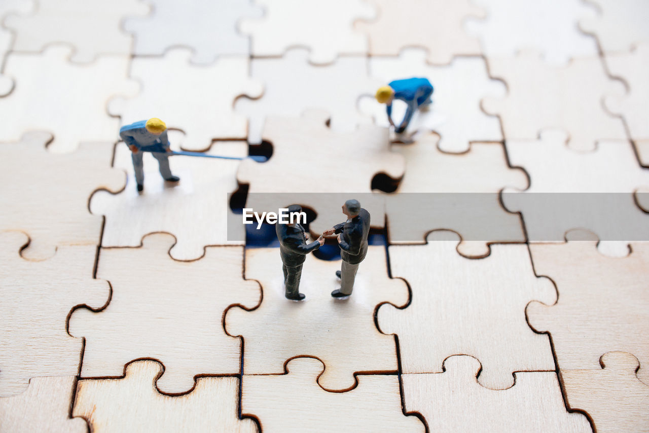 High angle view of figurines on wooden jigsaw puzzle