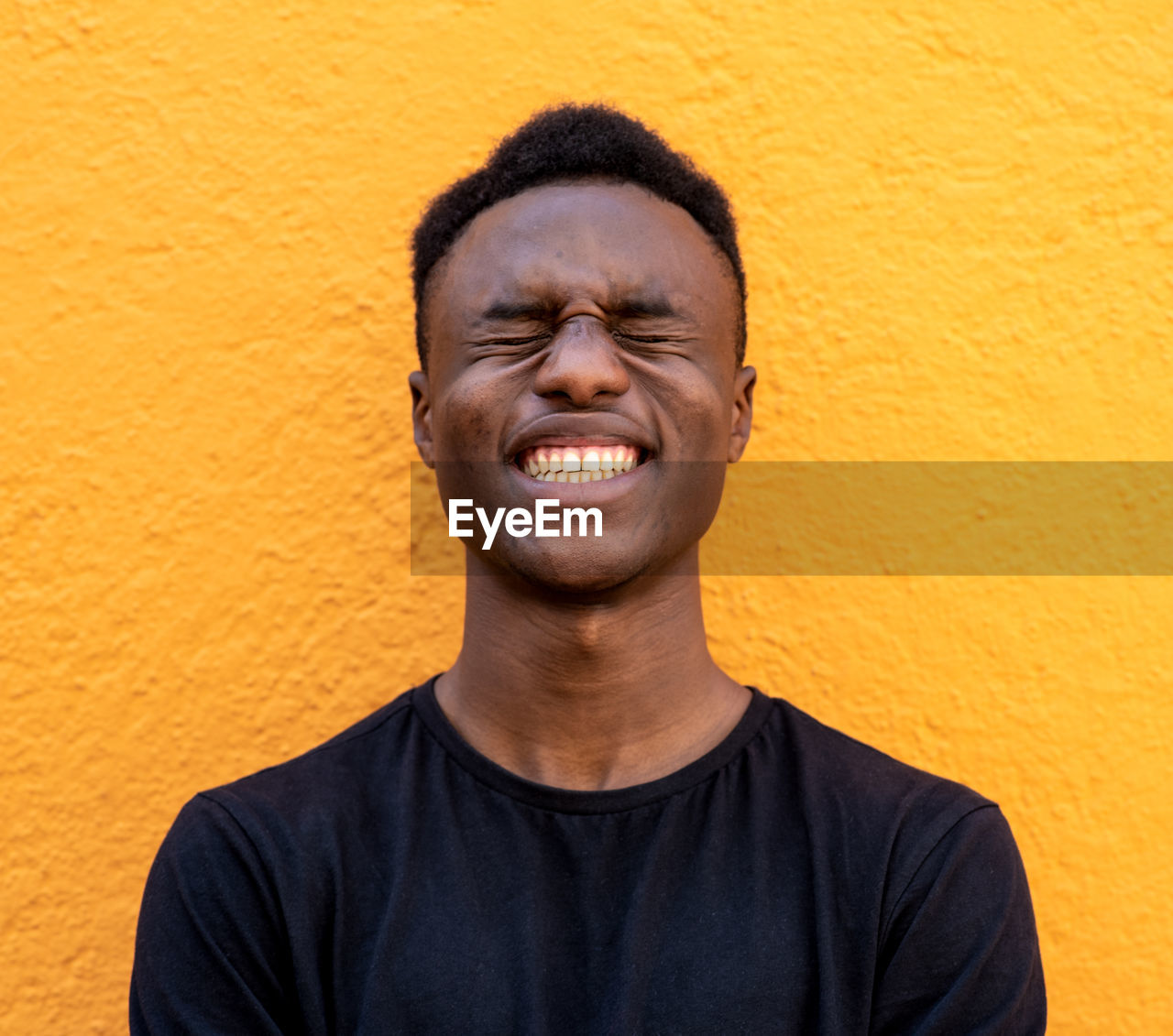 Smiling young man standing against yellow wall