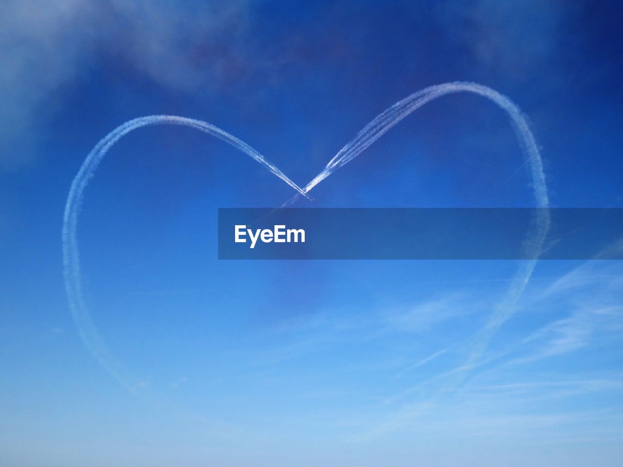Low angle view of vapor trails forming heart shape in blue sky