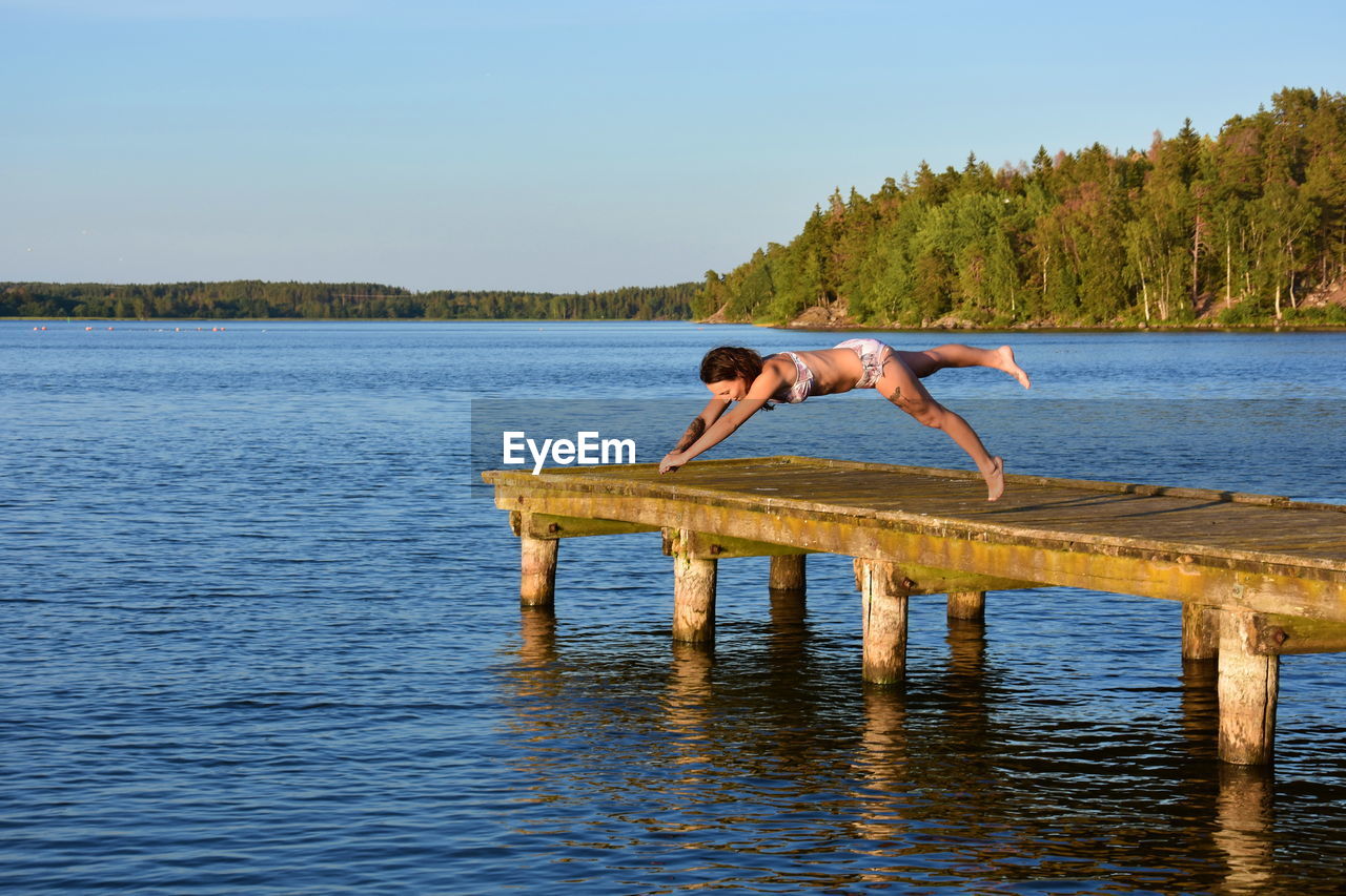 Side view of woman jumping in lake against sky