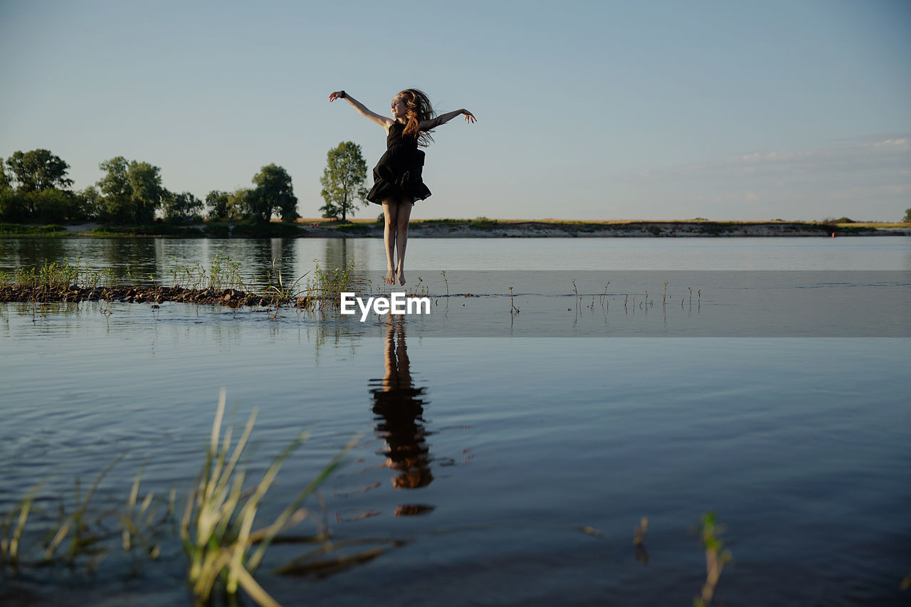 Teenage girl standing in lake against sky