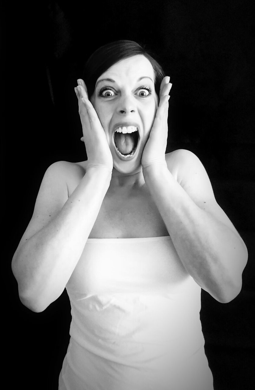 Portrait of woman with hand on cheek shouting against black background