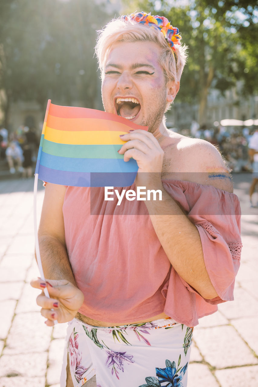 Happy gay man laughing with rainbow flag on sunny day