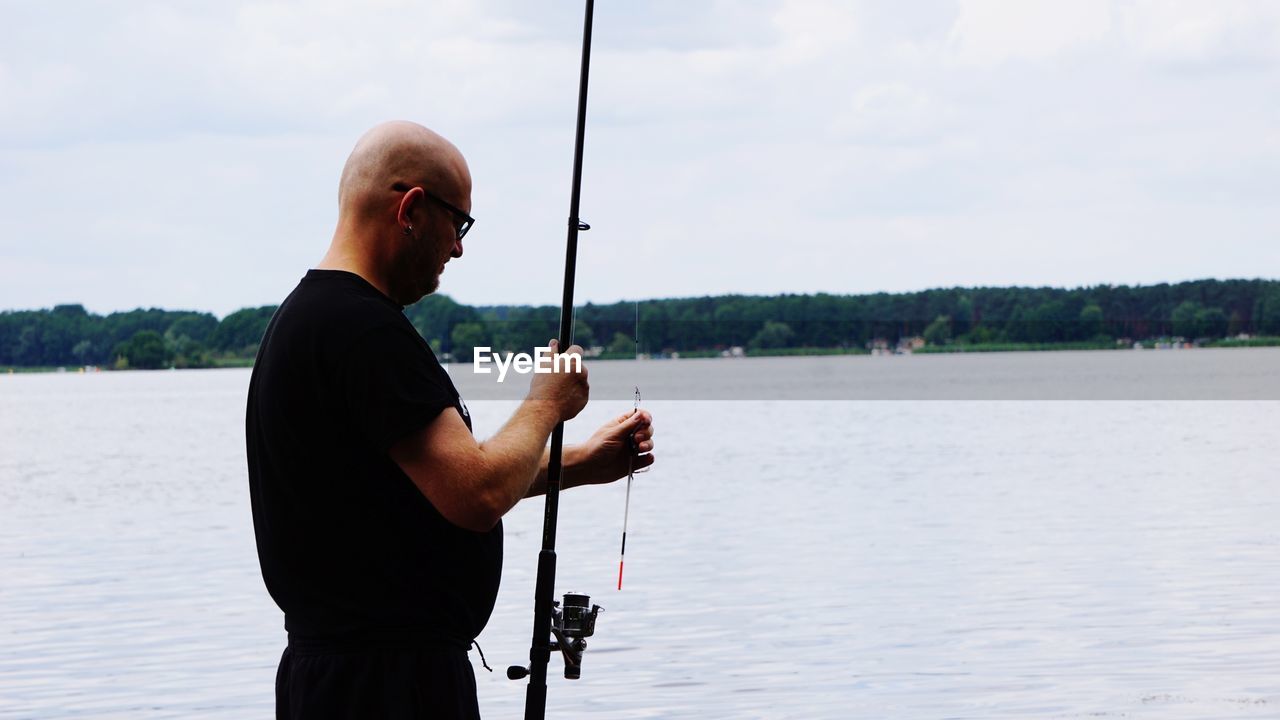 Bald man fishing in lake against sky