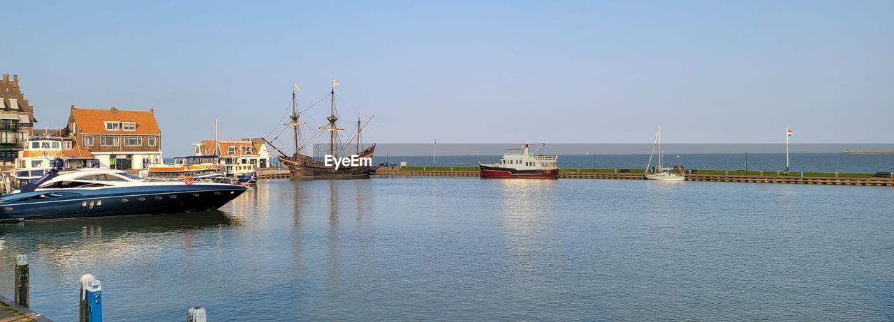 SAILBOATS MOORED IN HARBOR AGAINST CLEAR SKY