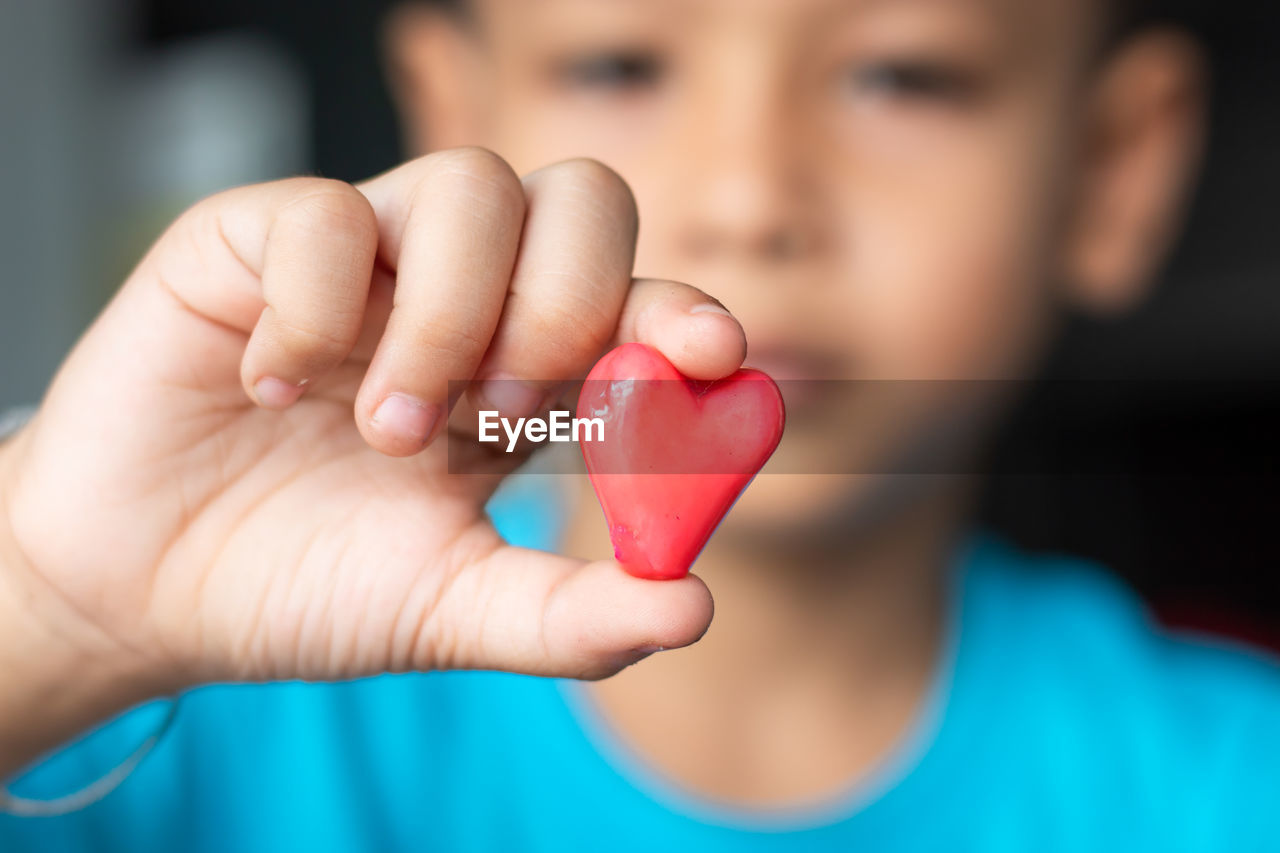CLOSE-UP OF BOY HOLDING HEART SHAPE WITH HAND