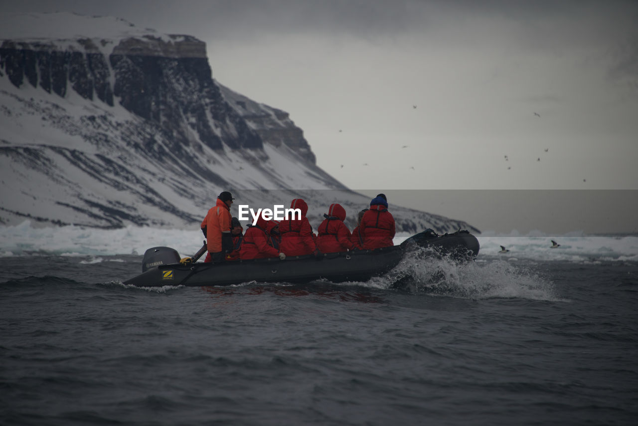 People rafting in river by snowcapped mountain against sky